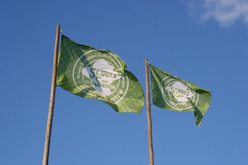 Twee groene vlaggen van Scouts en Gidsen ‘G. de Hasque’ Kluisbergen tegen een blauwe lucht